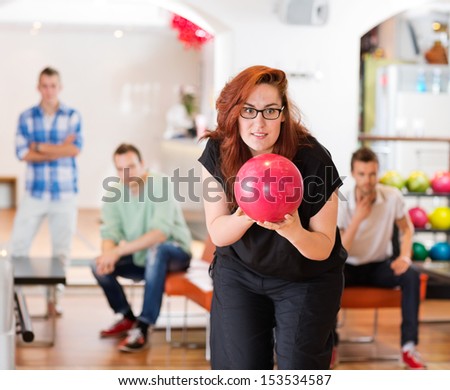 Young woman ready with bowling ball with friends in background at club