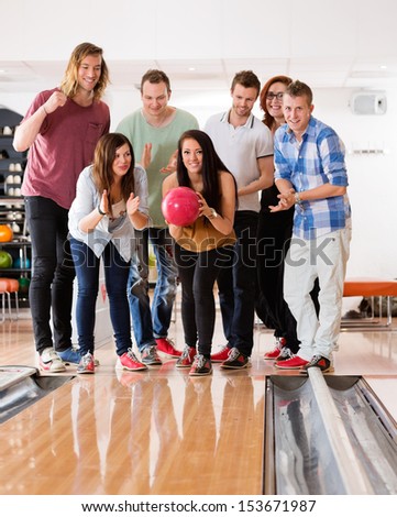 Young woman bowling while friends cheering in club