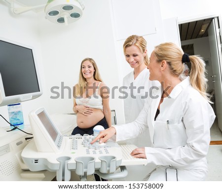 Gynecologists using ultrasound machine with pregnant woman sitting in clinic