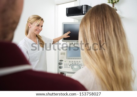 Young female gynecologist showing ultrasound machine\'s screen to expectant couple in clinic