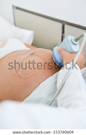 Closeup of obstetrician scanning pregnant belly by ultrasonic scan