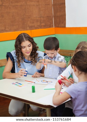 Young teacher with students painting at desk in kindergarten
