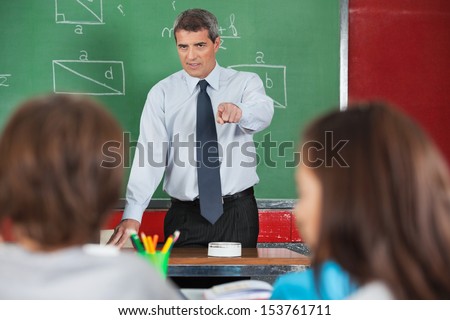 Angry male teacher pointing at students in classroom Angry male teacher pointing at students in classroom