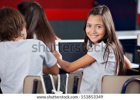 Side view portrait of schoolgirl holding digital tablet at desk in classroom