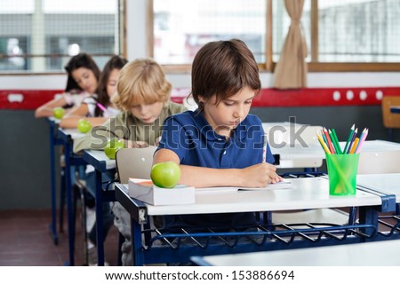 Elementary schoolchildren writing in books at desk in classroom