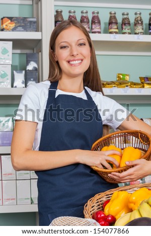 Portrait of beautiful young saleswoman holding vegetable basket in grocery store