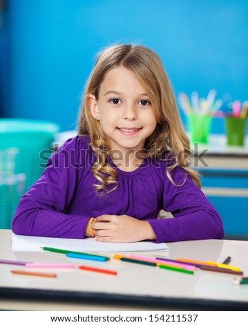 Portrait of cute little girl with colored sketch pens and paper in kindergarten
