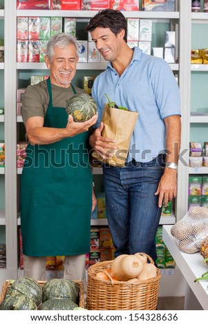 Happy senior salesman assisting male customer in buying vegetables at supermarket
