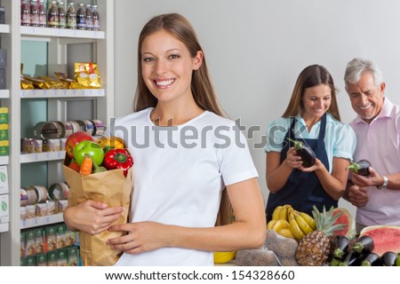 Portrait of young woman holding grocery bag while people shopping in background
