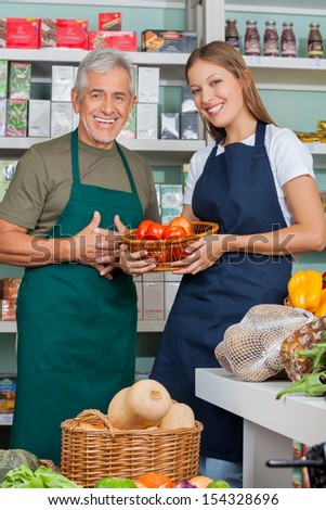 Portrait of saleswoman holding vegetable basket standing with male colleague in supermarket