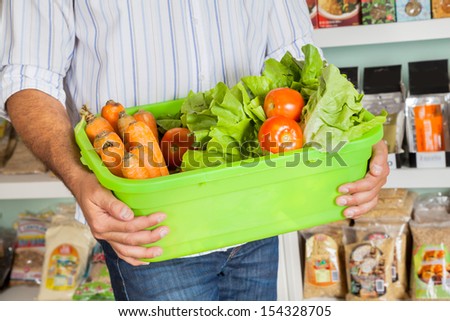 Midsection of mid adult man holding basket of fresh vegetables in supermarket