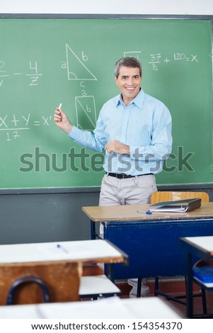 Portrait of happy male teacher teaching mathematics on board in classroom