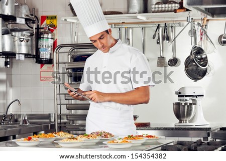 Young male chef using digital tablet with pasta dishes at kitchen counter