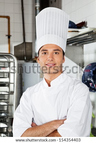Portrait of confident young chef with arms crossed in commercial kitchen