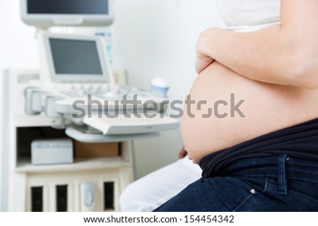 Midsection of pregnant woman with ultrasound machine in background at clinic