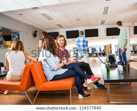 Young man and woman conversing while sitting on couch in bowling club