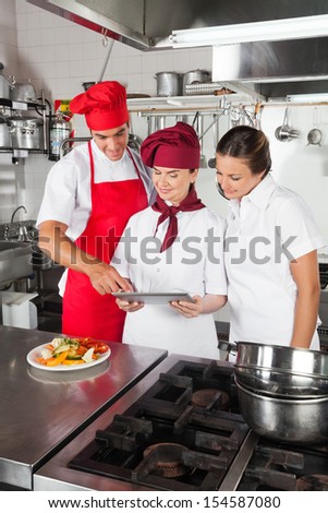 Three chefs looking for recipe on digital tablet in commercial kitchen