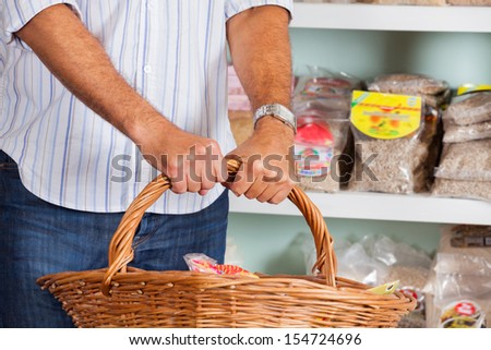Midsection of mid adult man holding wicker basket in supermarket