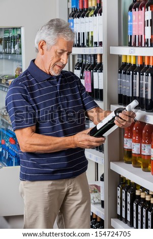 Senior man reading instructions from alcohol bottle at supermarket
