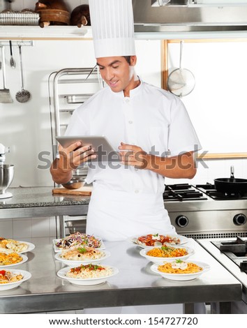 Happy chef using digital computer with pasta dishes on kitchen counter