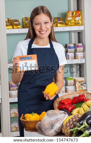 Portrait of young saleswoman holding pricetag and bellpepper in supermarket