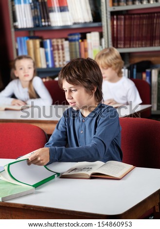 Little schoolboy studying at table in library