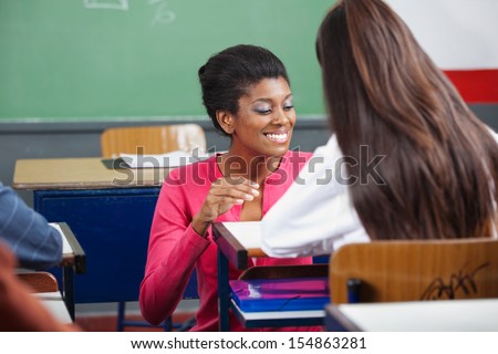 Young female teacher teaching teenage schoolgirl at desk in classroom