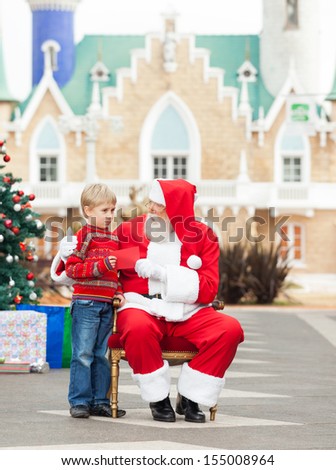 Full length of boy giving letter to Santa Claus against house