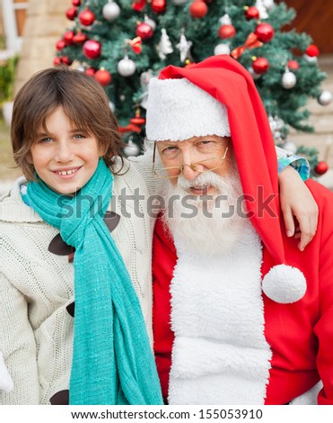 Portrait of happy boy with arm around Santa Claus against Christmas tree