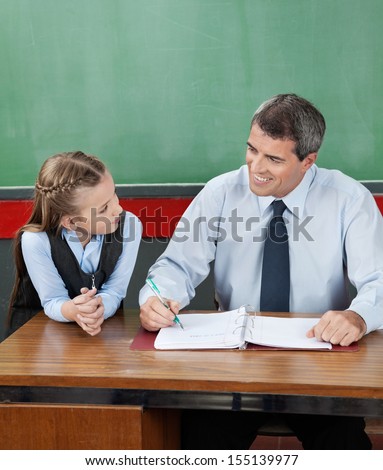Mature professor and little girl looking at each other at desk in classroom