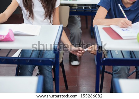 Midsection of schoolboy passing cheat sheet to girl during exam at desk in classroom