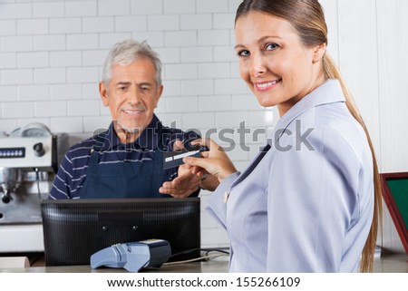 Portrait Of Mid Adult Woman Giving Credit Card To Male Cashier At Cash Counter