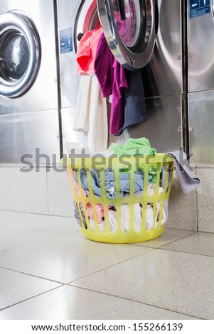 Overloaded washing machine with laundry basket on floor at laundromat