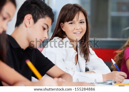 Portrait of teenage schoolgirl smiling with friends studying in classroom