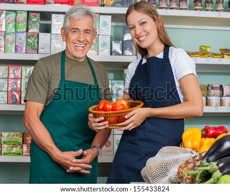 Portrait of saleswoman holding vegetable basket with male colleague in grocery store