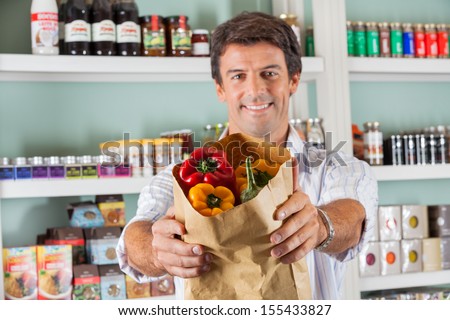 Portrait of happy man showing fresh bellpeppers in paper bag at grocery store