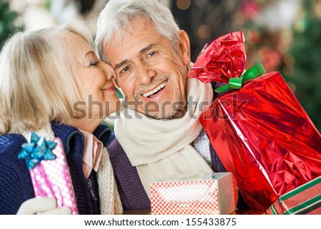 Romantic senior woman about to kiss man holding Christmas presents at store
