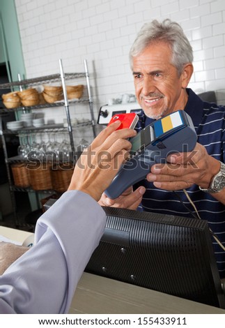 Senior salesman holding electronic reader while customer paying through smartphone