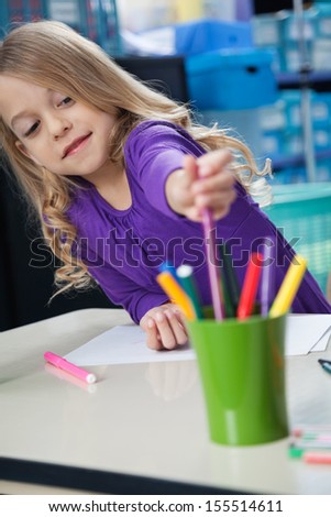 Cute little girl picking sketch pen from case at desk in classroom