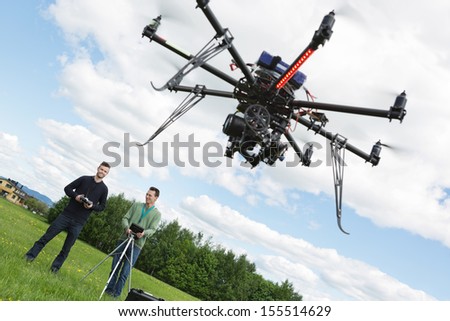 Young male engineers operating UAV helicopter against cloudy sky