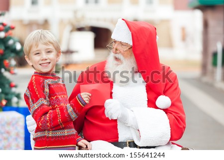 Portrait of happy boy giving letter to Santa Claus in courtyard