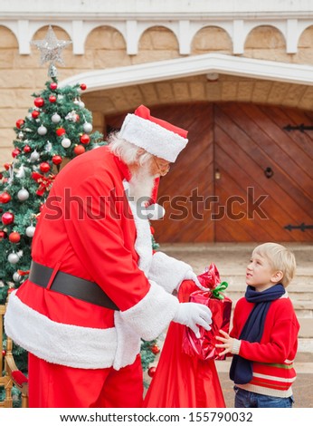 Boy looking at Santa Claus while taking gift from him against house