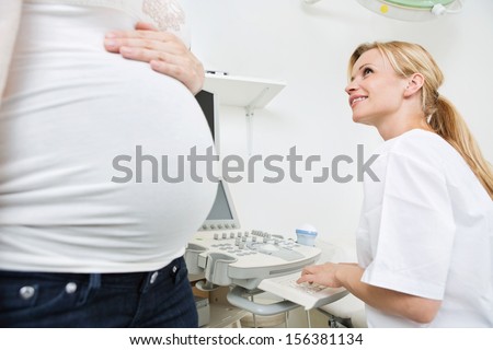 Young female doctor preparing for ultrasound scan while looking at pregnant woman in clinic