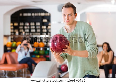Young confident man bowling with friends in background at club