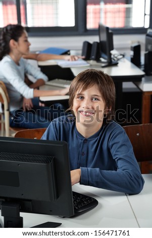 Portrait of happy schoolboy sitting with computer at desk in lab