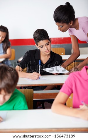 Young female teacher showing paper to university student during examination in classroom