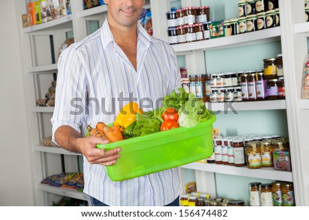 Midsection of mid adult man with basket of fresh vegetables standing in grocery store