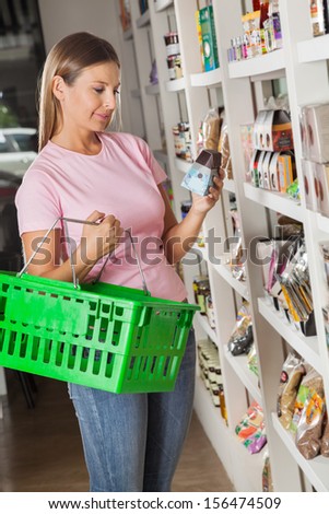 Beautiful mid adult woman with shopping basket choosing product in grocery store