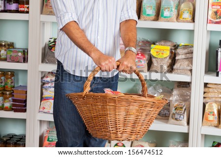 Midsection on mid adult man holding wicker basket against shelves in grocery store
