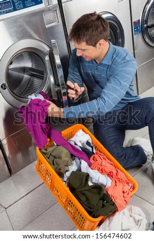 Young man putting clothes in washing machine at laundry